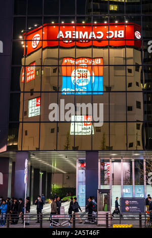 Tokyo, Akihabara. Chuo Dori street. Bic Camera superstore building reflected in the tinted windows of office block opposite. Evening. Pavement crowded Stock Photo