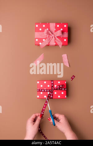 Woman hand cutting a ribbon and making gifts on brown background. Above view of gift wrapping concept. Christmas presents packaging. Birthday gifts. Stock Photo