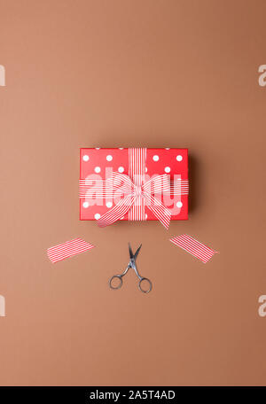 Festive red gift box and wrapping concept with bow and cut ribbon, on a brown background. Above view of Christmas gift and scissors. Birthday gift box Stock Photo