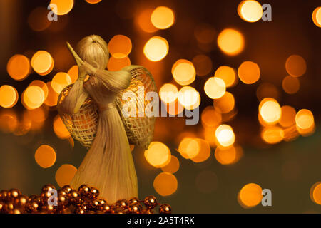 Straw angel praying on a blurred Christmas background. Beautiful bokeh created by Christmas lights. Traditional hand-made doll as a Christmas tree dec Stock Photo