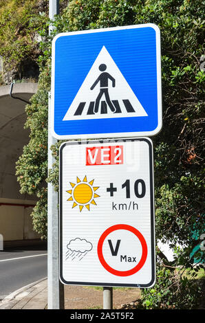 Road signs in Portuguese island Madeira. Blue zebra crossing sign. White speed limit sign. The speed restriction is dependent on weather, in case of clear weather the limit is plus 10 kmh than stated. Stock Photo