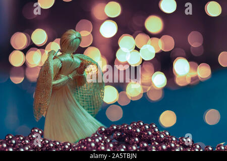 Straw angel praying on a blurred Christmas background. Beautiful bokeh created by Christmas lights. Traditional hand-made doll as a Christmas tree dec Stock Photo