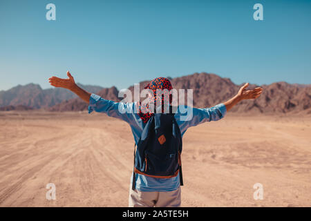 Tourist man with backpack raised arms feeling happy and free in Sinai Desert and mountains. Traveler admiring landscape. Summer vacation Stock Photo