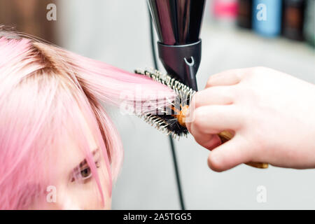 Hairdresser is drying pink hair with hair dryer and round brush. Hairdresser blow drying pink woman's hair close up. Stock Photo