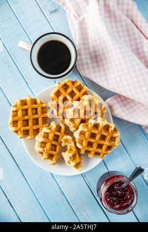Tasty sweet waffles with raspberry jam and tea cup on blue table. Top view. Stock Photo