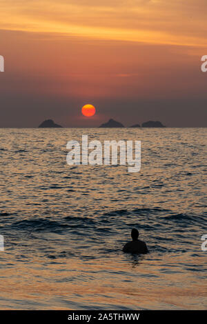 Sun setting on the Atlantic Ocean horizon between islands seen from Ipanema Beach in Rio de Janeiro, Brazil Stock Photo