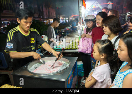 A crowd watches a man makes rolled ice-cream in Vietnam. Stock Photo