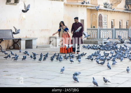 A young traditionally-dressed Indian couple feeds a flock of pigeons. Stock Photo