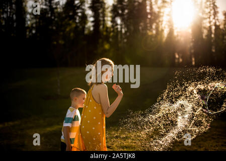 Siblings popping giant bubble in golden light Stock Photo