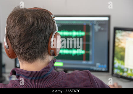 The man in the photo studio records and modifies singing, voice and music for commercial use. Works in an audio editor in a computer with headphone on Stock Photo