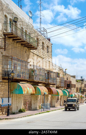 An Israeli armored vehicle passes in front of empty shops and buildings on Shuhada Street, which is closed to Palestinians. Hebron (al-Khalil), West B Stock Photo