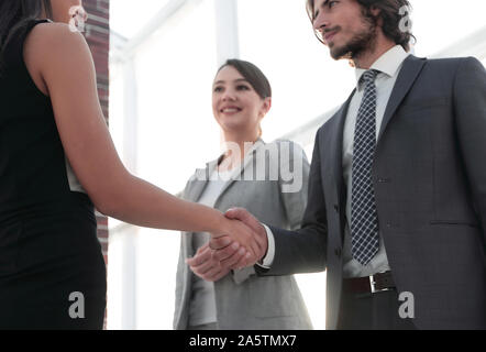 Businesspeople shaking hands against room with large window loo Stock Photo