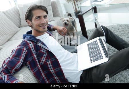 smiling young man with laptop sitting on the floor near the couch Stock Photo