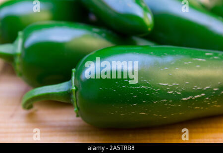 Close up photo of Jalapeño peppers (Capsicum annum) on a wooden surface. The jalapeno peppers are green and shiny. In the background blurred jalapeno. Stock Photo