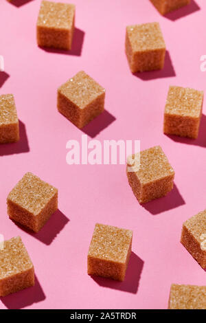 Geometry pattern made of brown sugar cubes on trendy pastel pink color background with hard shadows. Abstract,minimal style. Vertical orientation Stock Photo