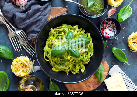 Pasta tagliatelle with pesto sauce and fresh basil liaves in black bowl. Top view with copy space. Stock Photo