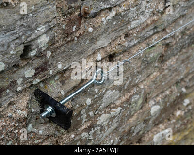 Vine eye and anchor plate for tensioning climbing plant support wire on an old stone wall Stock Photo
