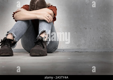 Young woman cries and sitting near a empty wall, lonely sad and depressed girl holding her head down Stock Photo