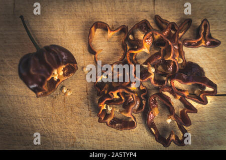 Chocolate Habanero pepper (Capsicum chinense) slices on a wood cutting board. Healthy and really hot chili peppers. Top view. Stock Photo
