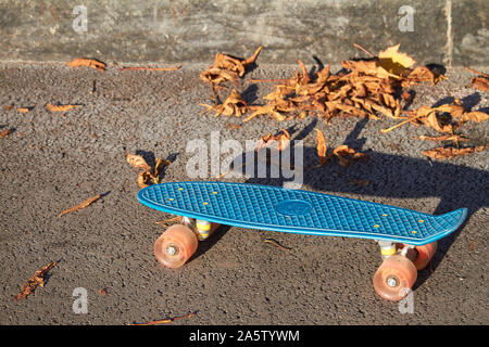 Abandoned blue skateboard on background of fallen foliage in the autumn park Stock Photo