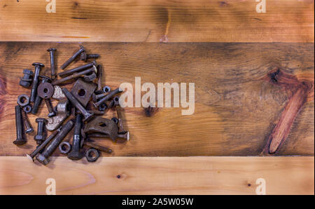 Wooden table background with rusty screws and bolts on the left side. Empty space on the right side. Top view. Stock Photo