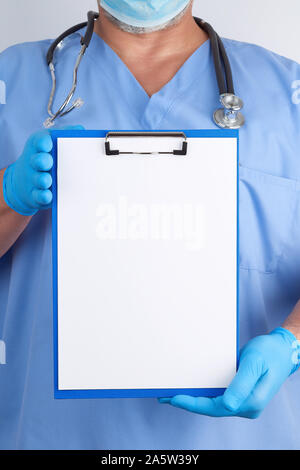 doctor in blue uniform and latex gloves holds a green holder for sheets of paper, empty space for writing text, white background Stock Photo