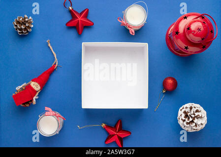 Empty gift box surrounded with Christmas decorations. Copy space on white gift box surface. Top view, flat lay, composition. Stock Photo