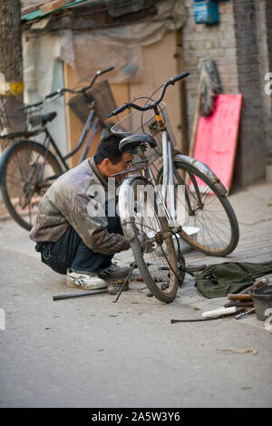 Mid-adult man fixing a bicycle on the side of a street. Stock Photo