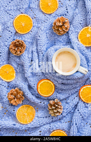 Winter mood composition. Cup of coffee, knitted blue blanket, dry oranges, pine cones. Flat lay, top view Stock Photo