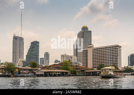 Bangkok city, Thailand - March 17, 2019: Chao Phraya River. Skyscrapers of offices and hotels around ruin of Old Customs House at quay. Iconsam shuttl Stock Photo