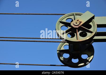 Rolling over metal, a steel cable stretches against a blue sky as background Stock Photo