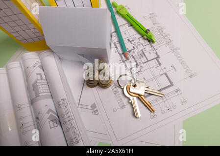 White family paper house , stack of money coins, keys, house projects plan and blueprints on mint background paper. Minimalistic and simple concept, s Stock Photo