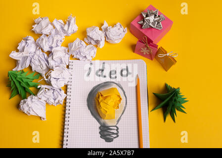 gift box and green paper origami trees with notepad on yellow desk, table. drawn yellow light bulb. Christmas idea concept. Stock Photo