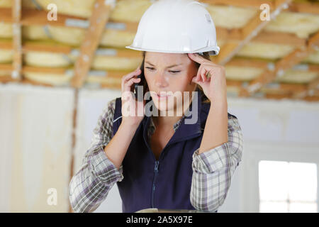 worried female builder using cellular telephone Stock Photo