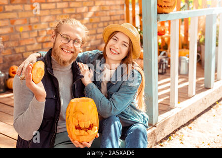 Halloween Preparaton Concept. Young couple sitting at porch with jack-o'-lantern hugging posing smiling cheerful Stock Photo