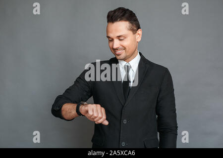 Businessman studio standing isolated on grey checking time on watch smiling Stock Photo