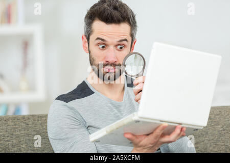 handsome man looking at his laptop through manifying glass Stock Photo