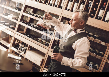 Sommelier Concept. Senior man standing stirring decanter with wine checking sediment Stock Photo