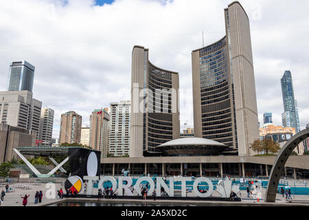 Toronto City Hall building and Toronto sign in Nathan Philips Square while tourists mingle around on a busy afternoon. Stock Photo
