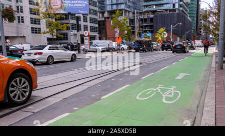Green bike lane on a busy street in downtown Toronto as a cyclist is seen in the distance. Stock Photo