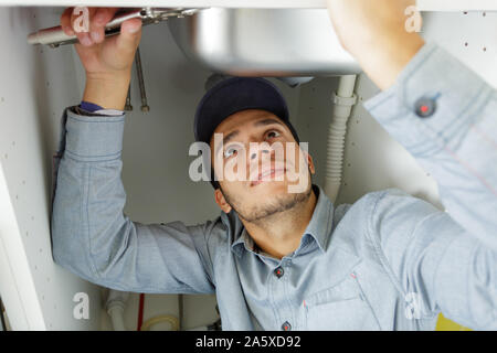 young male plumber performing a repair under the kitchen sink Stock Photo