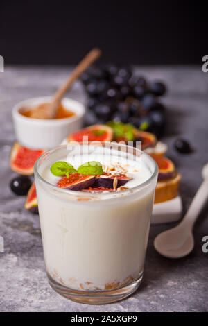 Yogurt with muesli and fig fruit, sandwich with cream cheese, figs and honey on the concrete background. Healthy food concept. Autumn harvest. Stock Photo
