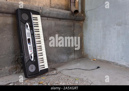 An abandoned old musical synthesizer stands near the wall of a building on the street Stock Photo