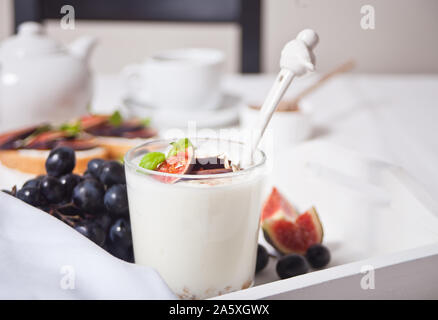 Yogurt with muesli and fig fruit, sandwich with cream cheese, figs and honey on the white tray. Healthy breakfast food concept. Stock Photo