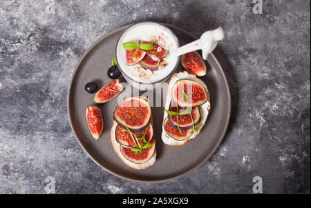Sandwich with cream cheese, figs and honey and yogurt in a glass served on the gray plate on the concrete background. Healthy food concept. Top view. Stock Photo