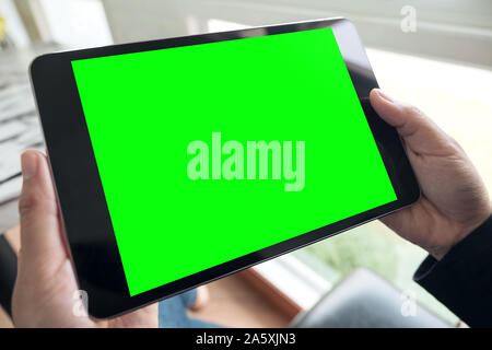 Mockup image of hands holding black tablet pc with blank green desktop screen in cafe Stock Photo