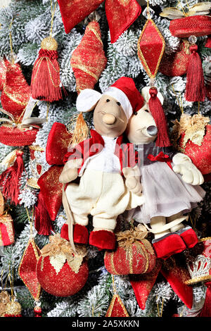 Pair of decorative toy mice is festively dressed in red clothes on the eve of the rat year on the background of the New Year tree. Stock Photo