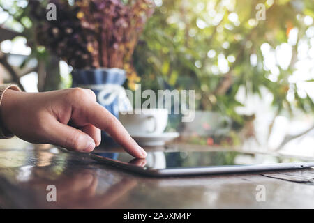 Closeup image of a woman's hand pointing , touching and using tablet pc on wooden table in cafe Stock Photo