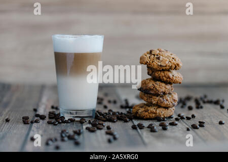 Caffe latte macchiato coffee layered with milk in a high drinking glass. The drink is on a wooden table with a pile of chocolate chip cookies next to Stock Photo
