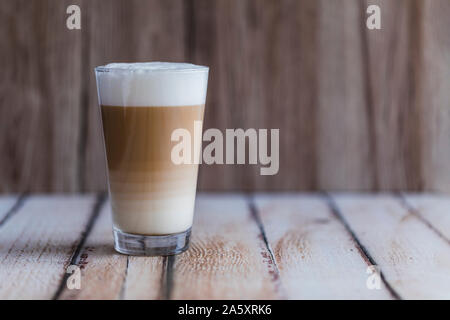 Caffe latte macchiato coffee layered with milk in a high drinking glass. There drink is on a wooden table with the background wooden as well. Empty sp Stock Photo